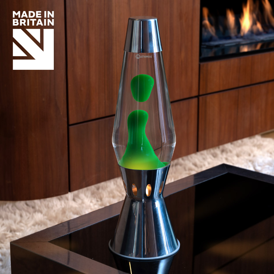 Lampe à lave à bougie Mathmos Astro Flame en argent avec liquide transparent et lave verte sur une table noire, avec une cheminée en arrière-plan
