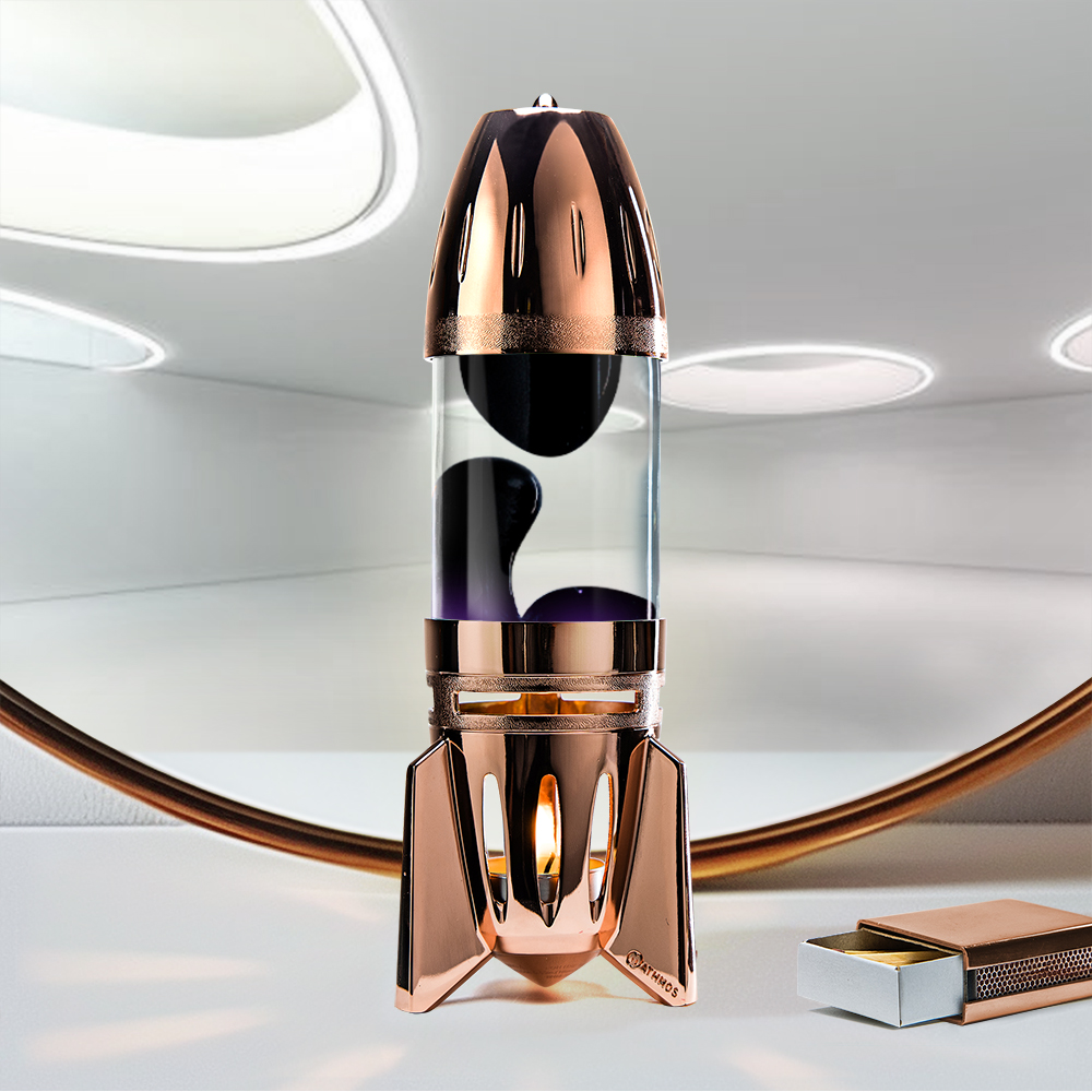 Lampe à lave à bougie en cuivre en forme de fusée Mathmos Fireflow avec liquide transparent et lave noire sur fond clair avec une boîte d'allumettes