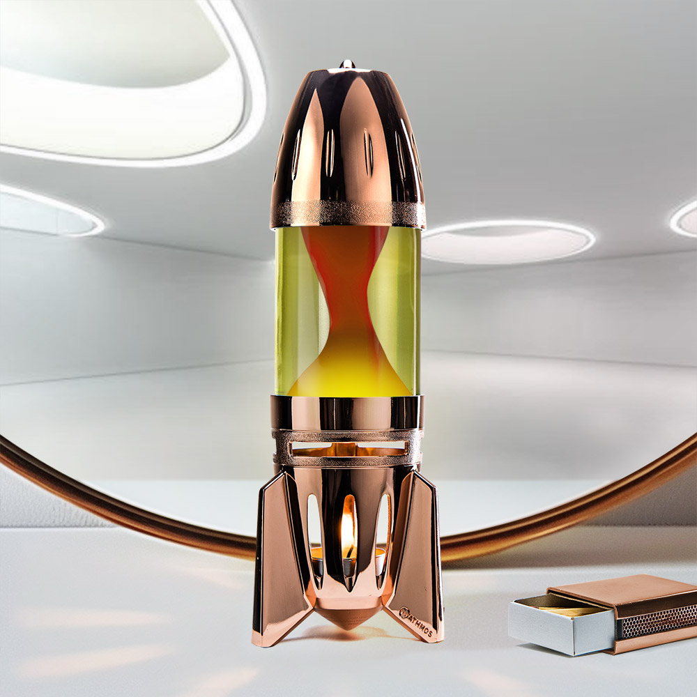 Lampe à lave à bougie en cuivre en forme de fusée Mathmos Fireflow avec liquide jaune et lave orange sur fond clair avec une boîte d'allumettes