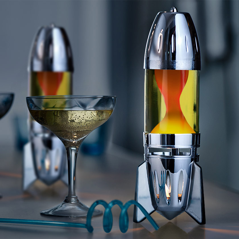 Lampe à lave à bougie Mathmos Fireflow avec corps argenté, liquide jaune et lave orange, posée sur une table dans un intérieur