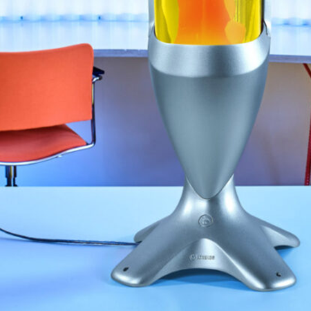 Partie inférieure d'une grande lampe à lave argentée Mathmos iO avec liquide jaune et lave orange sur une table bleu clair.