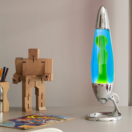Lampe à lave argentée Mathmos Neo avec liquide bleu et lave verte sur un bureau d'enfant à côté d'un robot jouet en bois et d'une bande dessinée.