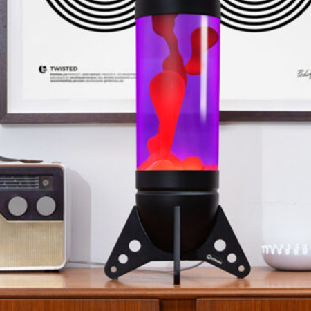 Grande lampe à lave noire Mathmos Rokit en forme de fusée avec liquide violet et lave rouge dans un intérieur de style rétro sur une armoire en bois.