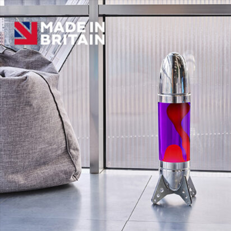 Grande lampe à lave argentée Mathmos Rokit en forme de fusée avec liquide violet et lave rouge posée sur le sol dans un intérieur clair.