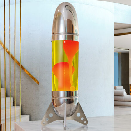 Grande lampe à lave argentée Mathmos Rokit en forme de fusée avec liquide jaune et lave orange dans un intérieur clair et moderne.